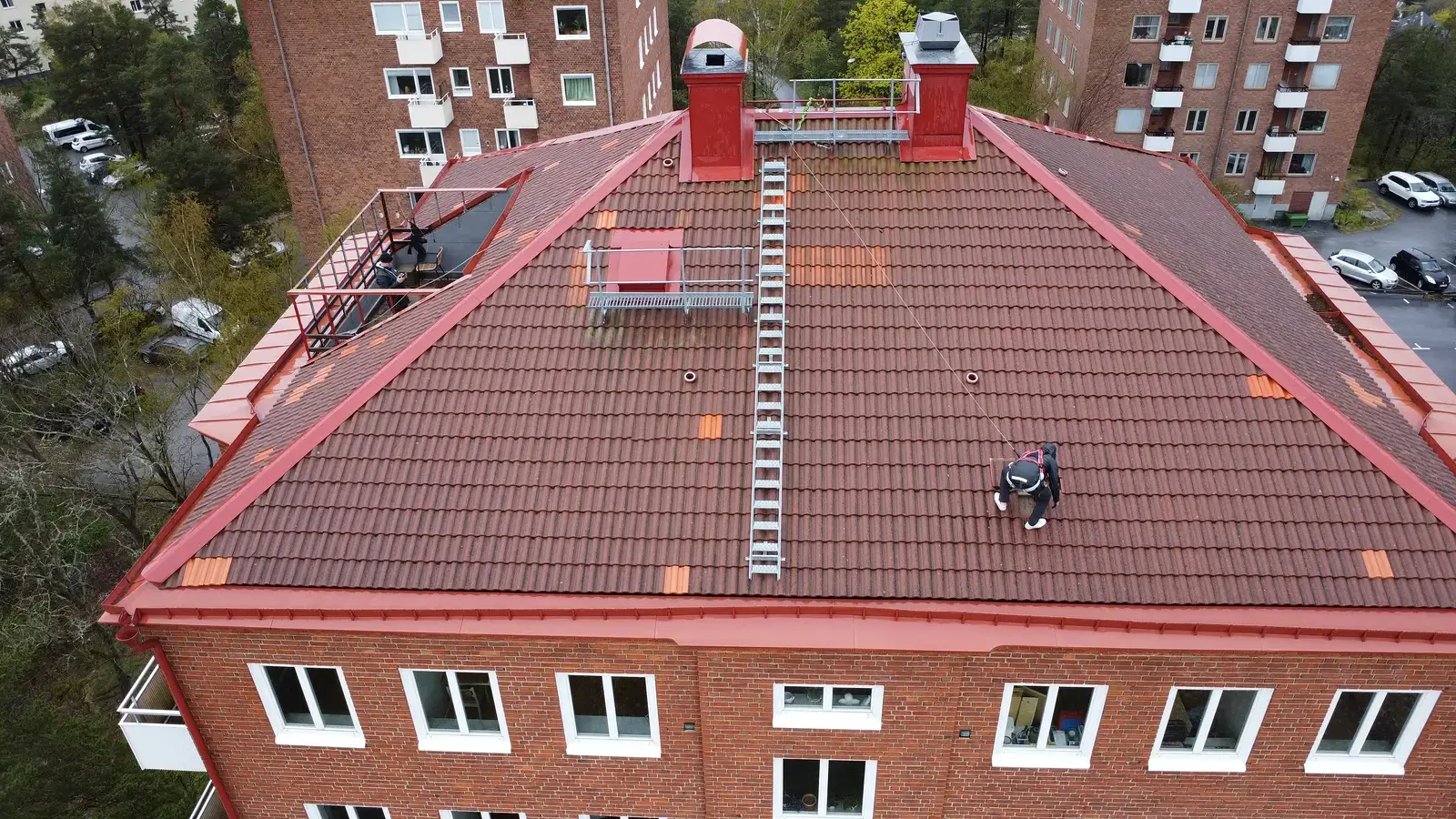 Takläggare arbetar på tegeltak på rött flervåningshus, drönarbild.